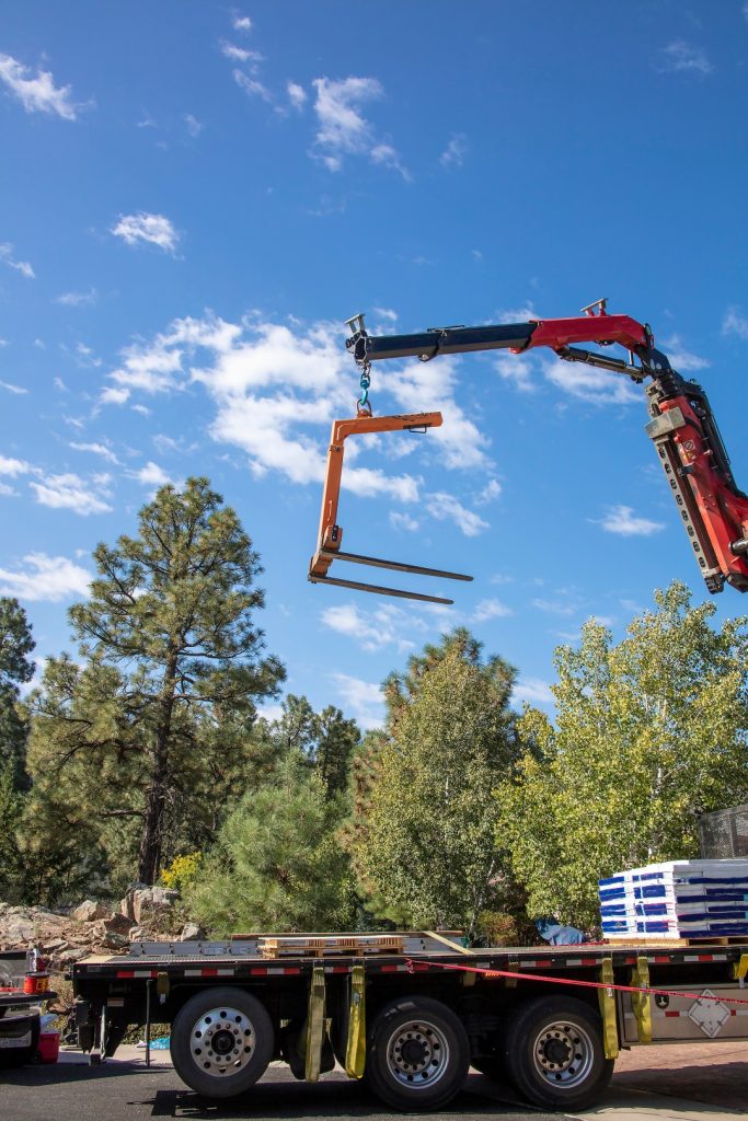 A bright yellow excavator loads dirt into a red dump truck on a construction site. The scene is under a partly cloudy blue sky, conveying industrious activity.